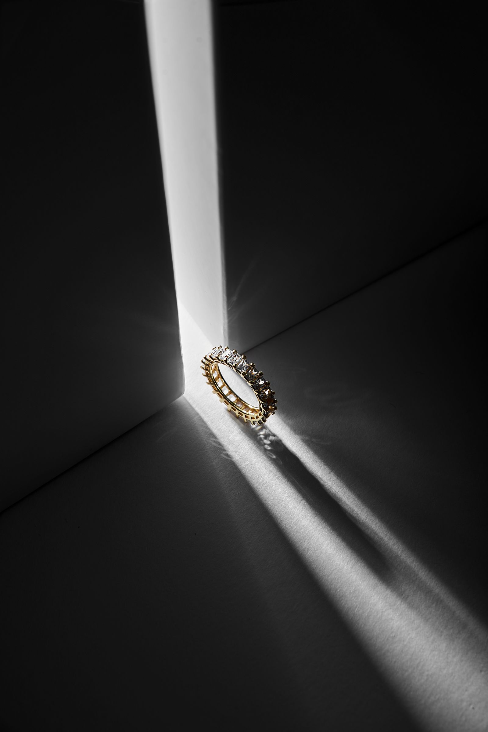 A gold diamond eternity band lit by a dramatic shaft of light against a dark background