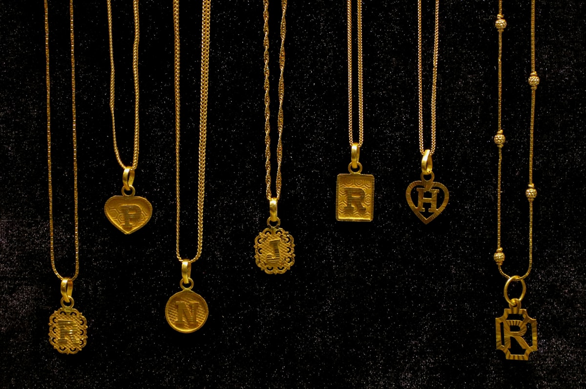 Several delicate gold necklaces with initial and symbol pendants displayed on white
