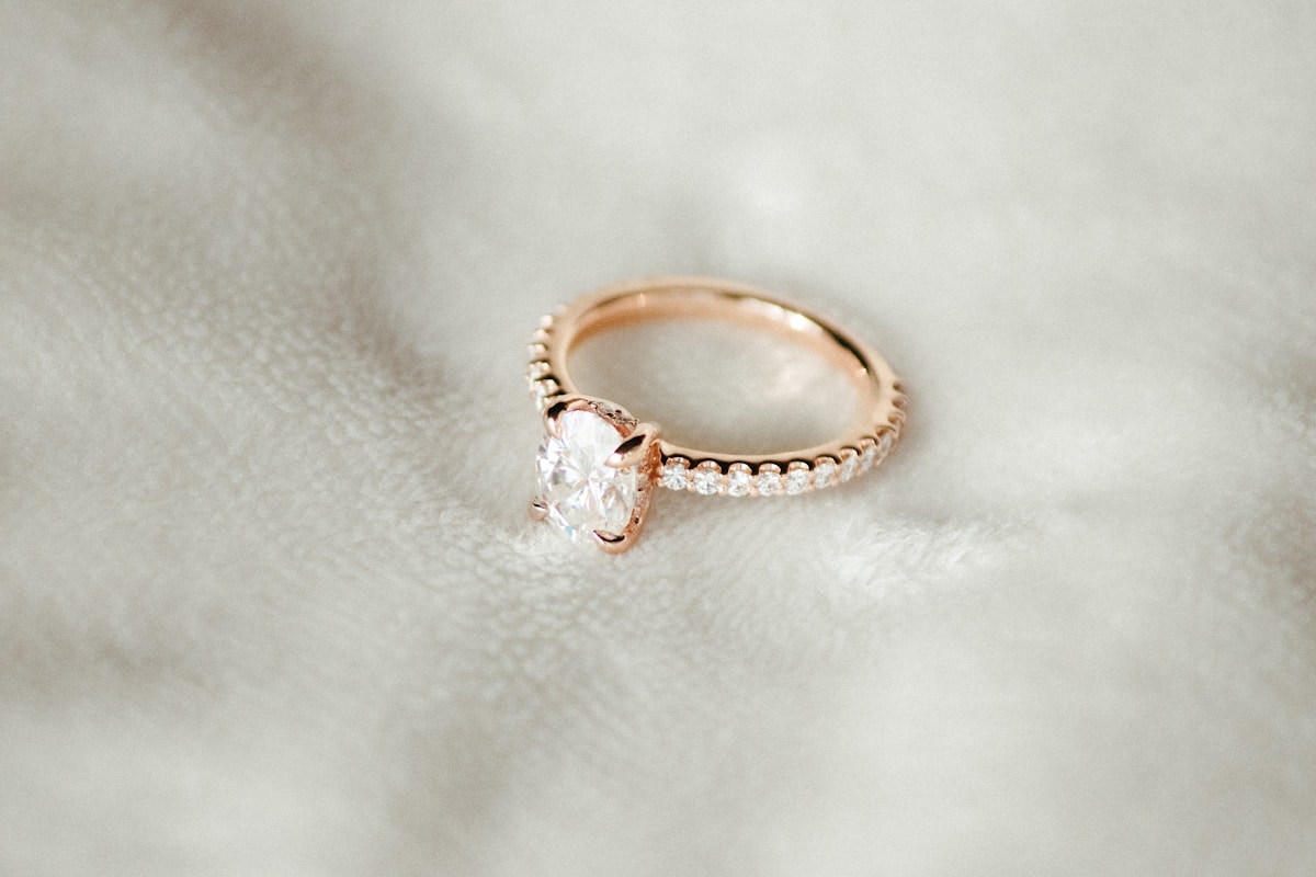 A rose gold ring with an oval diamond and a pavé diamond band on white fabric