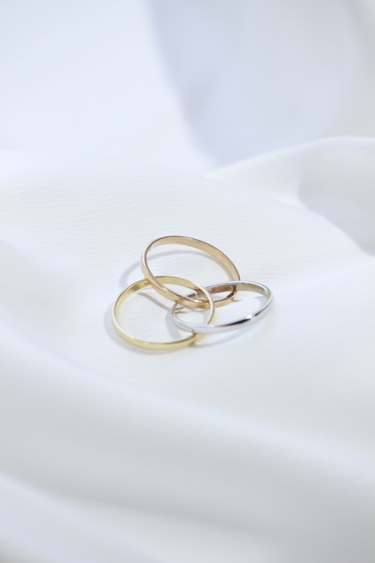 Three delicate interlocking gold and silver rings resting on white fabric