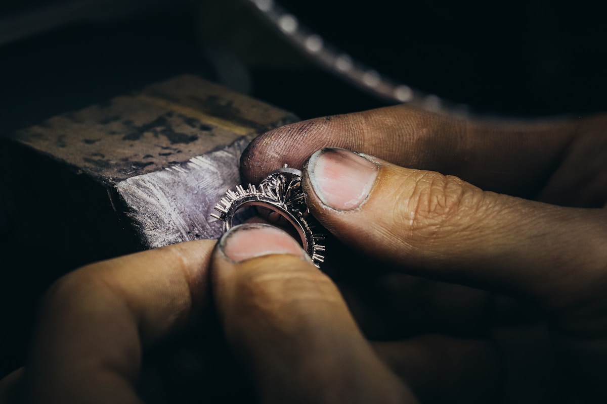 A jeweler's hands adjusting a diamond ring at a workbench