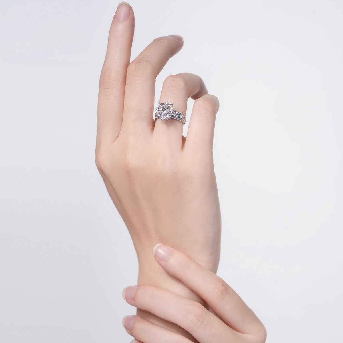 A woman's hand wearing a sparkling cluster engagement ring against a white background